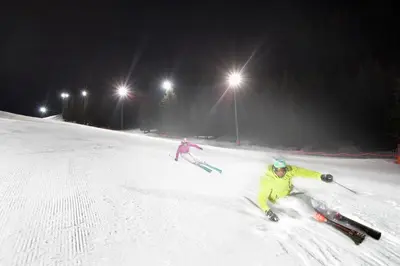two people skiing down a snow covered slope at night at Good Life Hotel Zirm in Obereggen