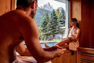 a man and a woman sitting in front of a window at Hotel Terme Antico Bagno in Pozza di Fassa