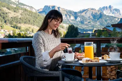 a woman sitting at a table with food and drinks at Hotel Terme Antico Bagno in Pozza di Fassa