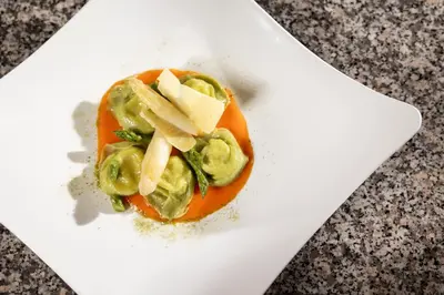 a white plate with a tomato with cheese and vegetables at Hotel Terme Antico Bagno in Pozza di Fassa