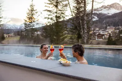 two people in a swimming pool with drinks at Hotel Terme Antico Bagno in Pozza di Fassa