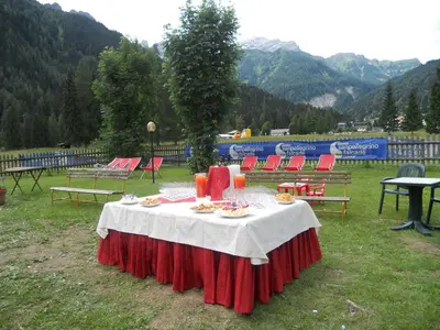 a table in a field with red chairs and a table with food on it at Hotel Stella Alpina in Falcade