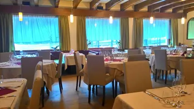 a restaurant with white tables and chairs and windows at Hotel Stella Alpina in Falcade