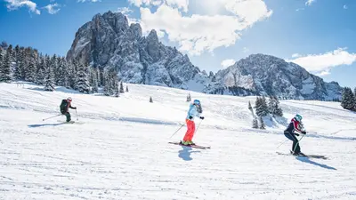 three people are skiing down a snow covered mountain at SAN PIETRO DOLOMITI Small Budget Hotel in Ortisei