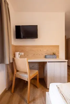 a room with a desk with a television on a wall at SAN PIETRO DOLOMITI Small Budget Hotel in Ortisei