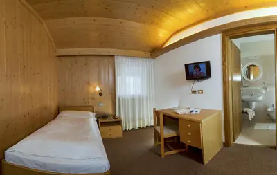 a bedroom with a bed and a desk and a sink at Hotel Gran Mugon in Vigo di Fassa