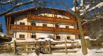 a large wooden house with a fence in the snow at Hotel Mair Am Bach in Bressanone