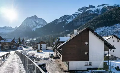 a small building in a village with snow covered mountains at Residence Contrin in Canazei