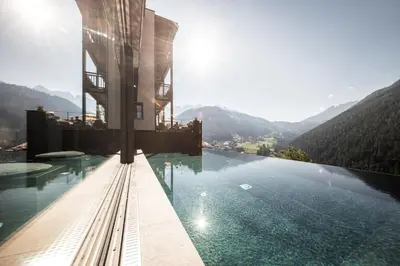 a hotel with a infinity pool with mountains in the background at Charme Hotel Friedrich in Nova Levante