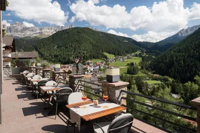 a restaurant with tables and chairs on a balcony with mountains at Charme Hotel Friedrich in Nova Levante