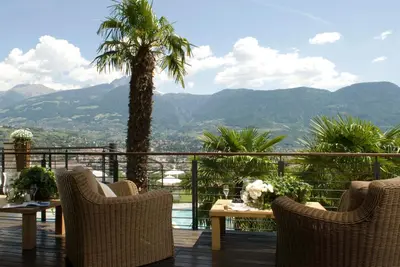 a balcony with chairs and a table and a palm tree at Giardino Marling in Merano