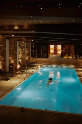 a person swimming in a swimming pool at night at Rosapetra SPA Resort - Small Luxury Hotels of the World in Cortina dʼAmpezzo