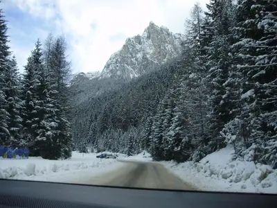 a car driving down a snow covered road with a mountain at Hotel Villa Cima Undici in Pozza di Fassa