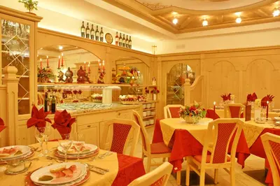 a dining room with tables and chairs and a kitchen at Hotel Villa Cima Undici in Pozza di Fassa