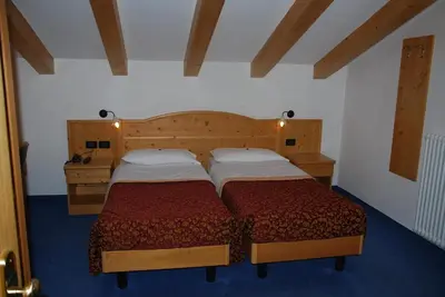 two twin beds in a room with blue carpet at Hotel El Geiger in Pozza di Fassa