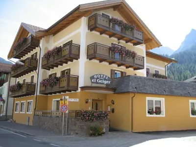 a large yellow building with balconies on a street at Hotel El Geiger in Pozza di Fassa