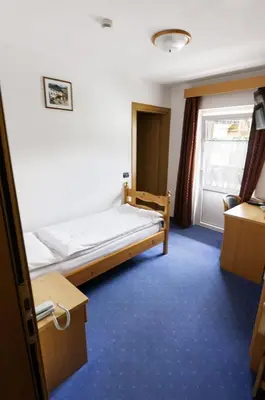a small room with a bed and a window at Hotel El Geiger in Pozza di Fassa
