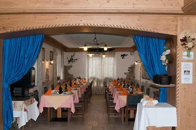a dining room with tables and blue drapes at Hotel El Geiger in Pozza di Fassa