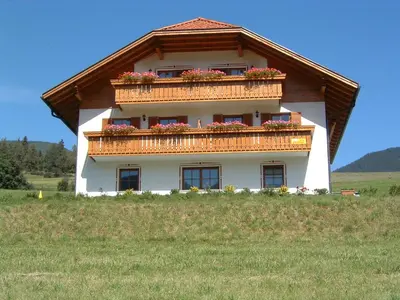 a house with a balcony on top of a field at Stegerhof in Monguelfo