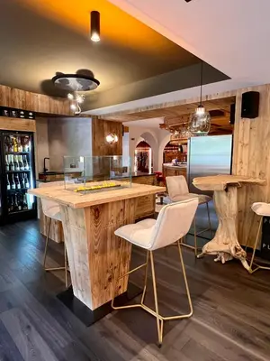 a kitchen with a bar with white chairs and wooden floors at Albergo Conturina in Canazei
