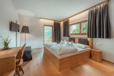 a bedroom with a bed and a desk and window at Gailerhof Boutique Hotel B&B Dolomites in Monguelfo