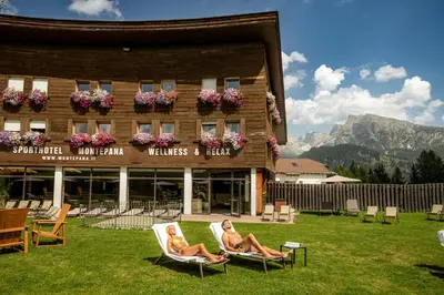 two women sitting in lawn chairs in front of a building at Monte Pana Dolomites Hotel in Santa Cristina in Val Gardena