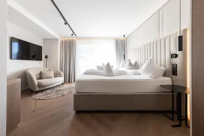 a bedroom with a large white bed and a chair at Hotel Prokulus - Family & Wellness in Naturno
