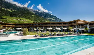 a hotel with a pool and mountains in the background at Hotel Prokulus - Family & Wellness in Naturno