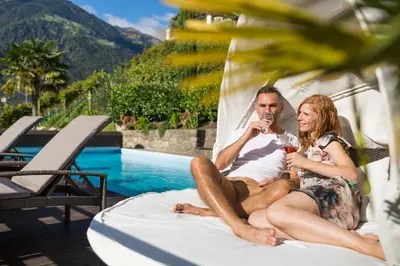 a man and woman sitting on a bed next to a pool at Hotel Weingut Innerleiterhof in Schenna