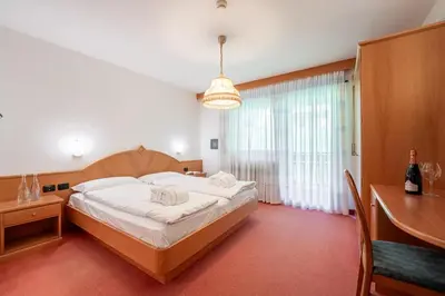 a bedroom with a bed and a table and a window at Hotel Dolomites Inn in Canazei