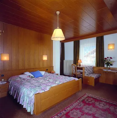 a bedroom with a bed and a chair and a window at Hotel Garni Soreie in Pozza di Fassa