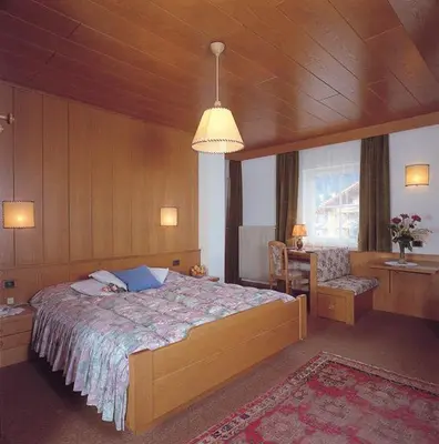 a bedroom with a large bed and a desk and a window at Hotel Garni Soreie in Pozza di Fassa