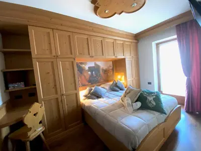 a bedroom with a bed with wooden cabinets and a window at Hotel Laurino in Pozza di Fassa