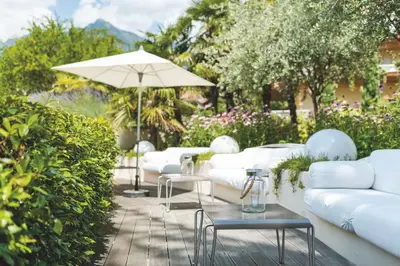 a patio with white couches and an umbrella at Hotel Mignon Meran Park & Spa in Merano