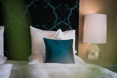 a bed with a blue pillow and a lamp on it at Hotel Mignon Meran Park & Spa in Merano