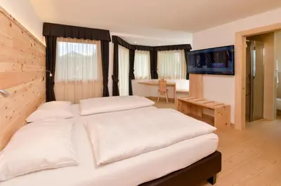 a bedroom with a large white bed and a television at Hotel Silvana in Selva di Val Gardena