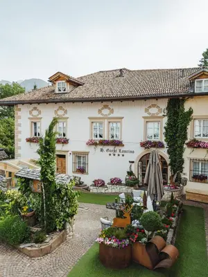 a large white house with a garden in front of it at Bio Boutique Hotel Laurino in Cavalese