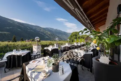 a restaurant with tables and chairs with mountains in the background at Hotel Rössl in Rablà