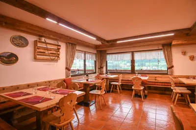 a restaurant with wooden tables and chairs and windows at Hotel El Laresh in Moena