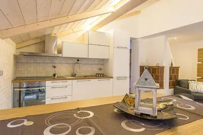 a kitchen with white cabinets and a living room at Mansarda Ciliegio Cavalese in Cavalese