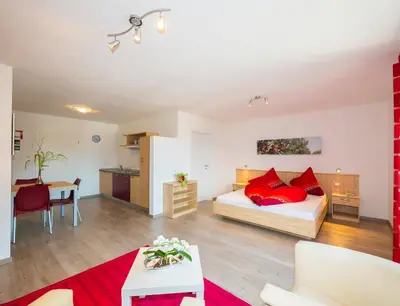 a bedroom with a bed with red pillows and a kitchen at Gasserhof Garni & Apartment in Schenna
