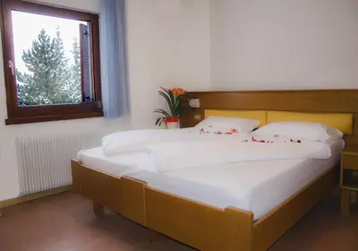 a bedroom with a bed with white sheets and a window at Hotel Casa Alpina - Alpin Haus in Selva di Val Gardena