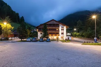 a large building with cars parked in a parking lot at Hotel Casa Alpina - Alpin Haus in Selva di Val Gardena