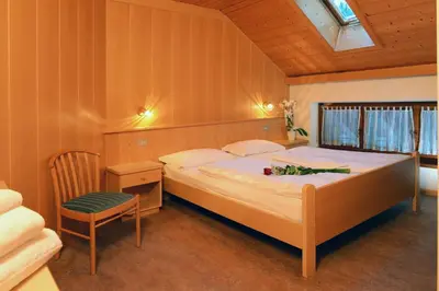 a bedroom with a large bed and a chair at Hotel Casa Alpina - Alpin Haus in Selva di Val Gardena