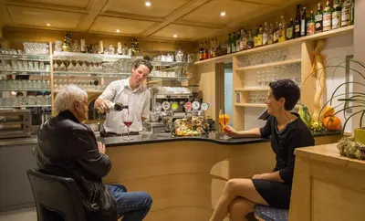 three people sitting at a bar with a bartender at Drei Birken in Soprabolzano