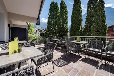 a group of chairs and tables on a patio with trees at Vitaurina Royal Hotel in Molini di Tures