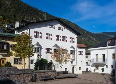a large white building with red windows and a mountain at Hotel Ansitz Kandelburg in Mühlbach