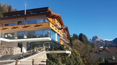 a house on a hill with mountains in the background at Hotel Garnì Gardena - Appartments in Santa Cristina in Val Gardena