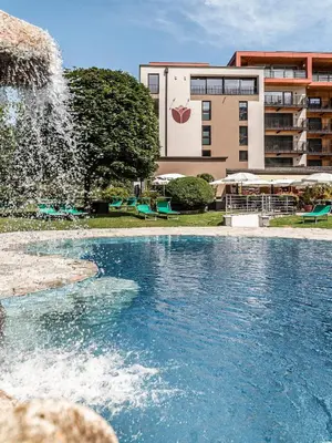a swimming pool with a fountain in front of a building at Hotel Olympia in Brunico