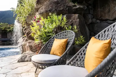 two wicker chairs with yellow pillows next to a fountain at Hotel Olympia in Brunico